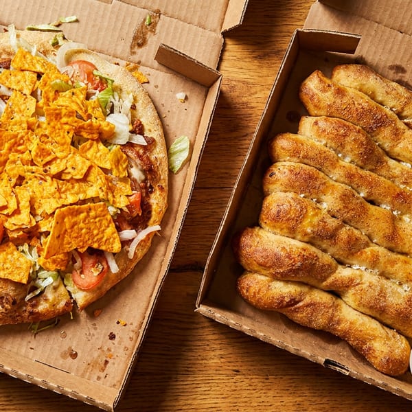 Taco pizza topped with tortilla chips and a box of breadsticks with dipping sauces.