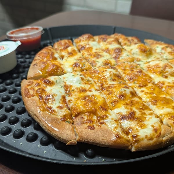 Cheesy breadsticks with marinara and garlic dipping sauces on a black tray.