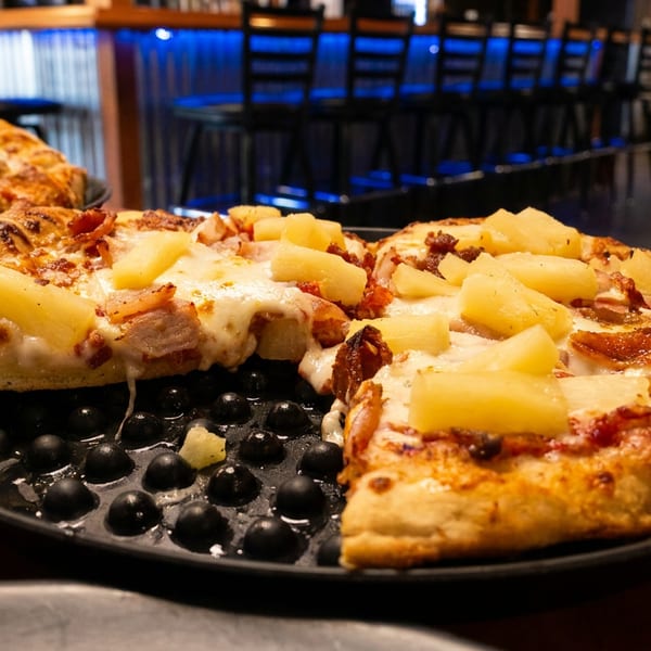 Hawaiian pizza with pineapple and ham, with a slice being served in a restaurant setting.