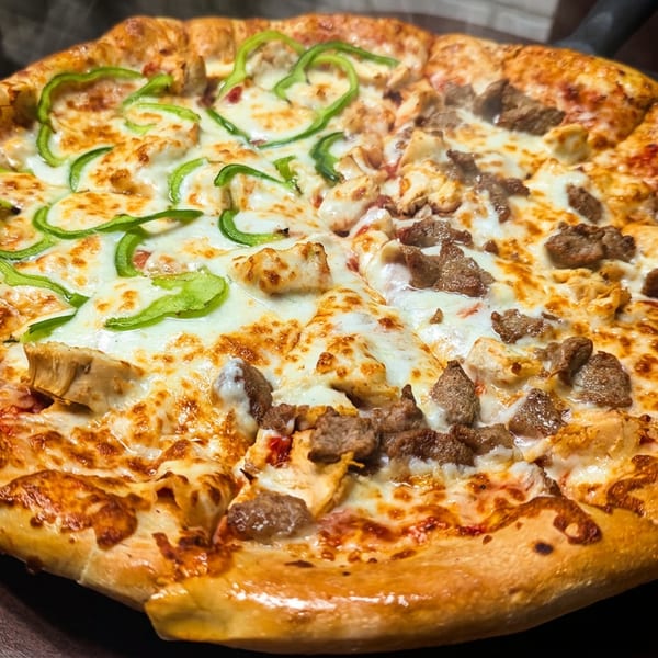 A whole pizza with half topped with green bell peppers and chicken, and the other half with beef.